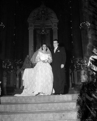 Novios de pie frente a imagen religiosa, en una iglesia, retrato