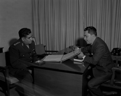 Ejecutivo le muestra documento a militar en una oficina q
