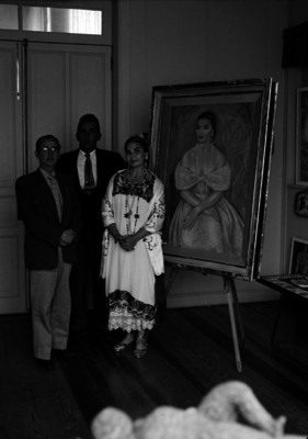 Melida de la Selva acompañada de dos hombres, posando junto a una pintura