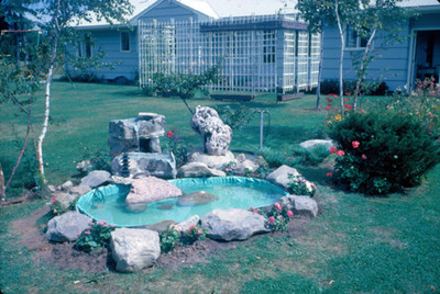 Fuente decorada con piedras en un jardin, al fondo la casa