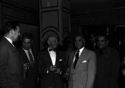 Harry H. Steel conviviendo con varios hombres y militar, durante un evento en un salón