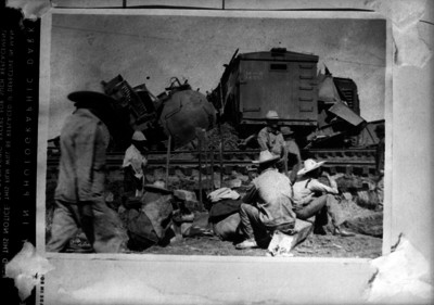 Ferrocarrileros descansando junto a una vía y vagones accidentados