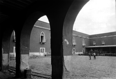 Hombres cargan barril en el patio de una hacienda