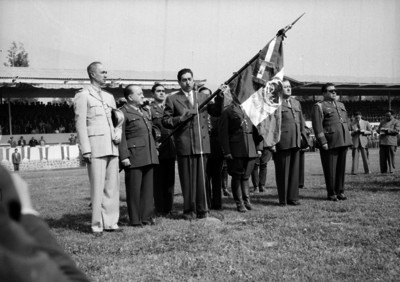 Miguel Alemán Valdés sosteniendo una bandera del Colegio Militar en una ceremonia