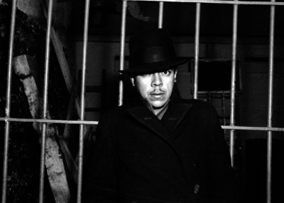 Detenido con sombrero y gabardina en una celda, retrato
