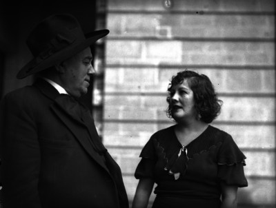 José Ma. Gutiérrez, corbatón, dialogando con una mujer a las afueras de un edificio