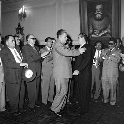 Adolfo López Mateos y Fidel Velázquez Sánchez abrazándose durante la audiencia con delegados de la convención de la CTM en un salón